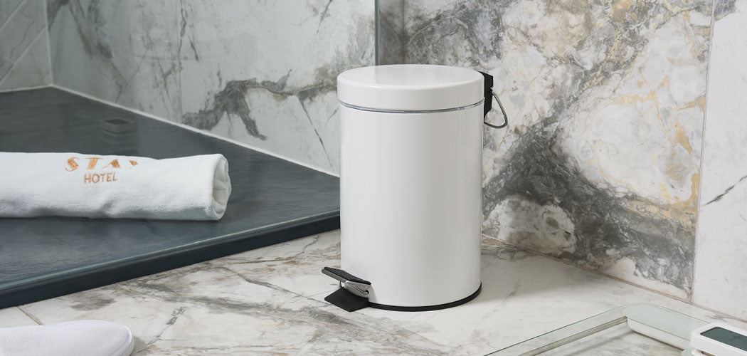White pedal bin in luxury marble hotel bathroom next to walk-in shower, towel, slippers, and digital scale