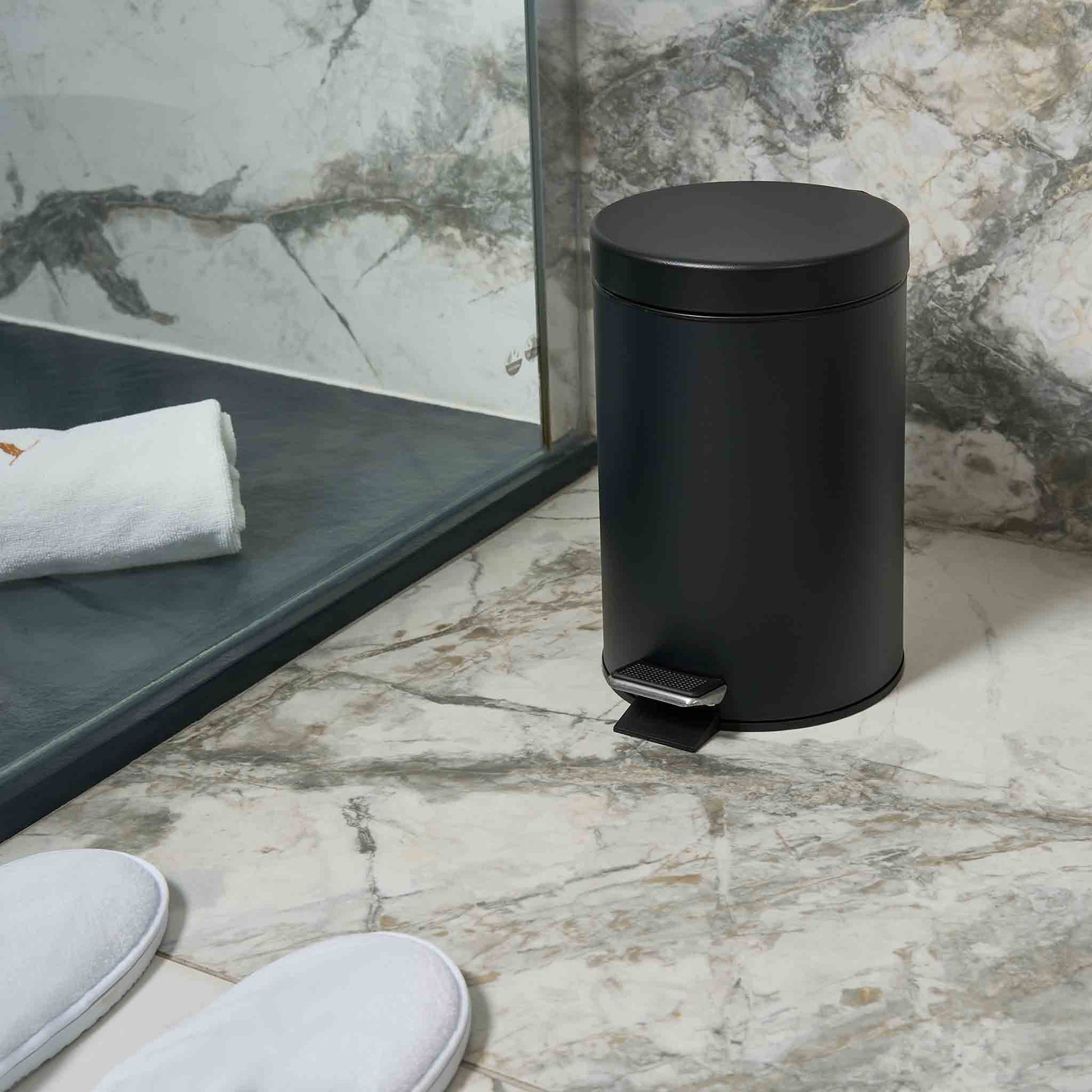 Corby Croft 3 litre black pedal bin placed beside walk-in shower in marble hotel bathroom with slippers and towel