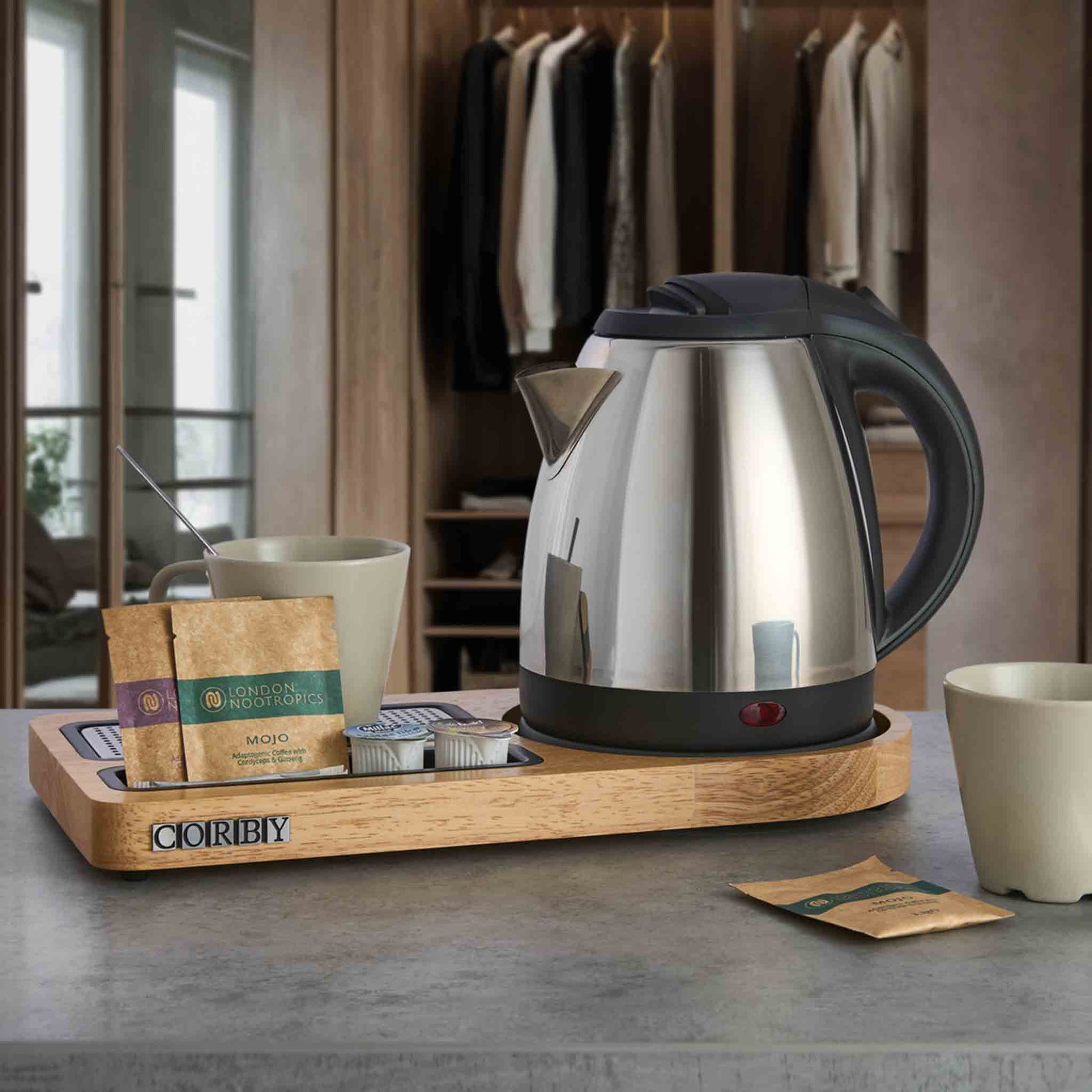 Corby Buckingham chrome hotel kettle on wooden hospitality tray with mugs, stirrer, and hot drink sachets in guest room setting