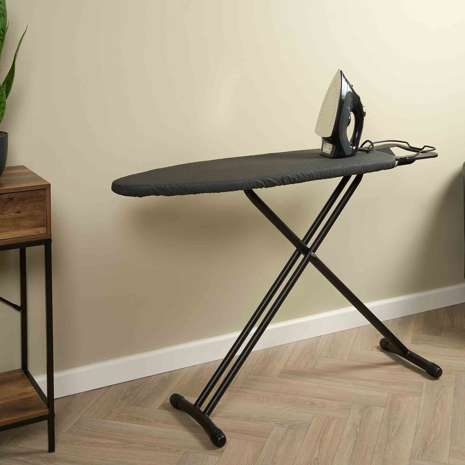 Corby Classic dark grey ironing board with iron rest shown in guest room setting with steam iron