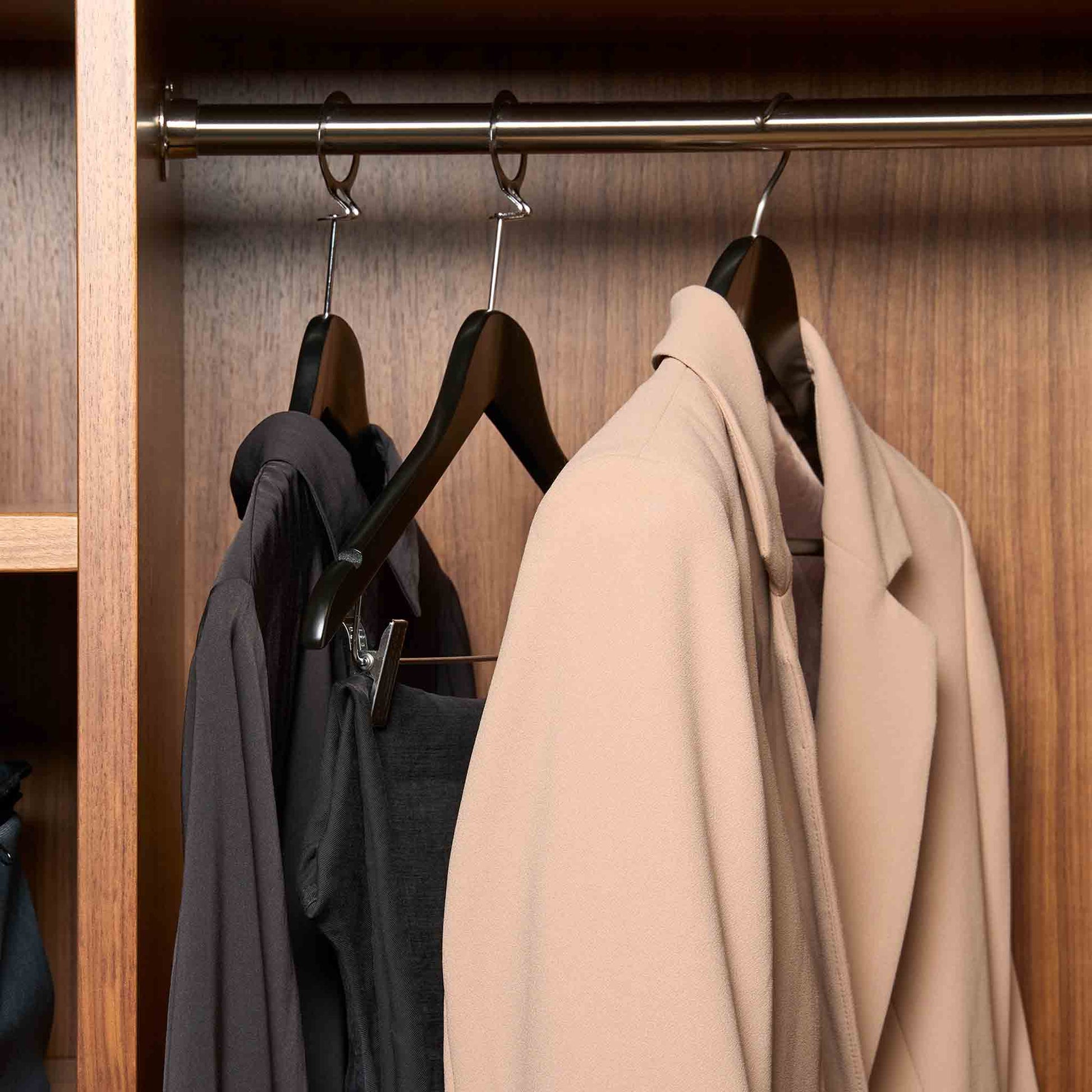 Corby Clifford black wooden suit hangers with chrome hooks holding guest clothing in hotel wardrobe