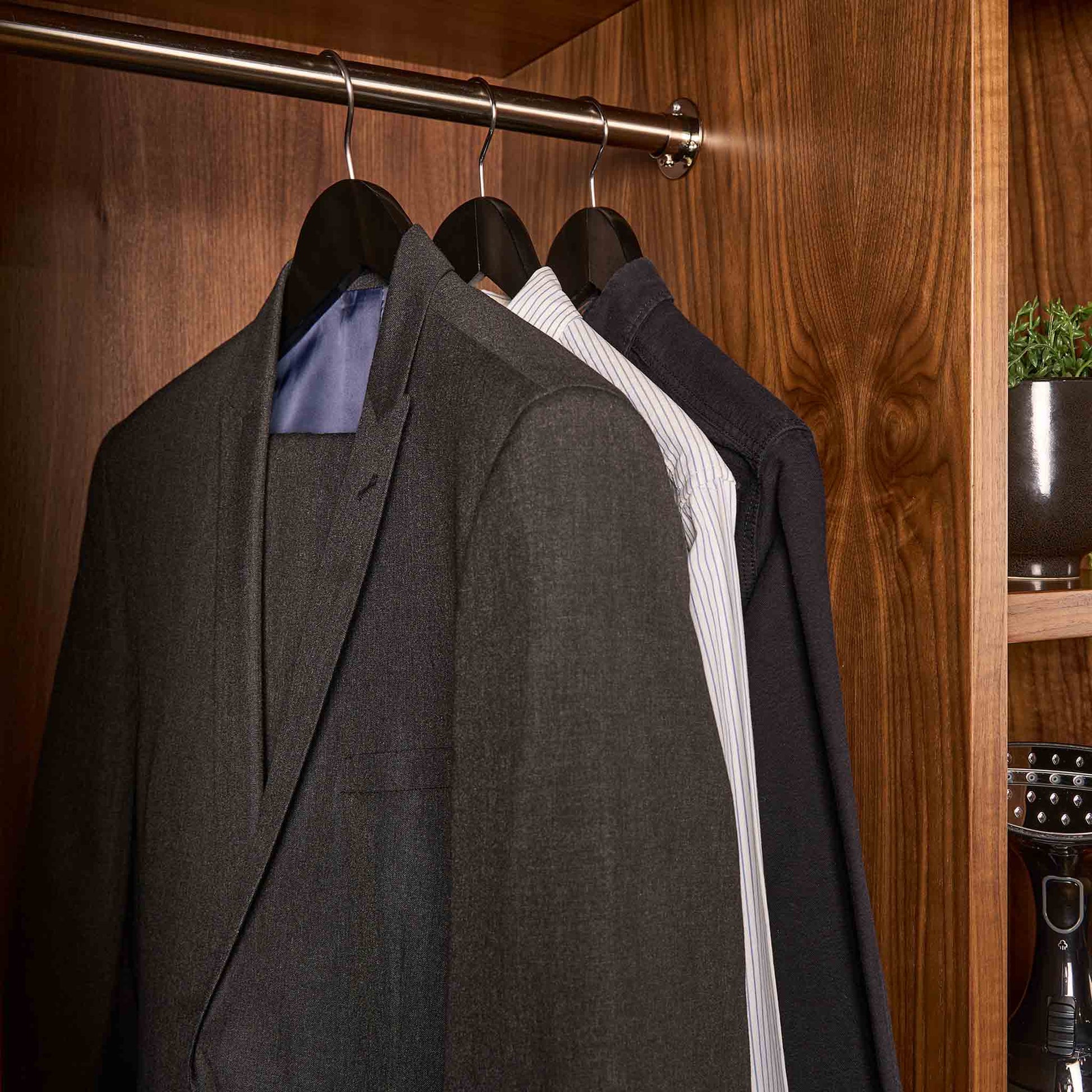 Corby Clifford black wooden suit hangers holding guest clothing in luxury hotel wardrobe with chrome rail