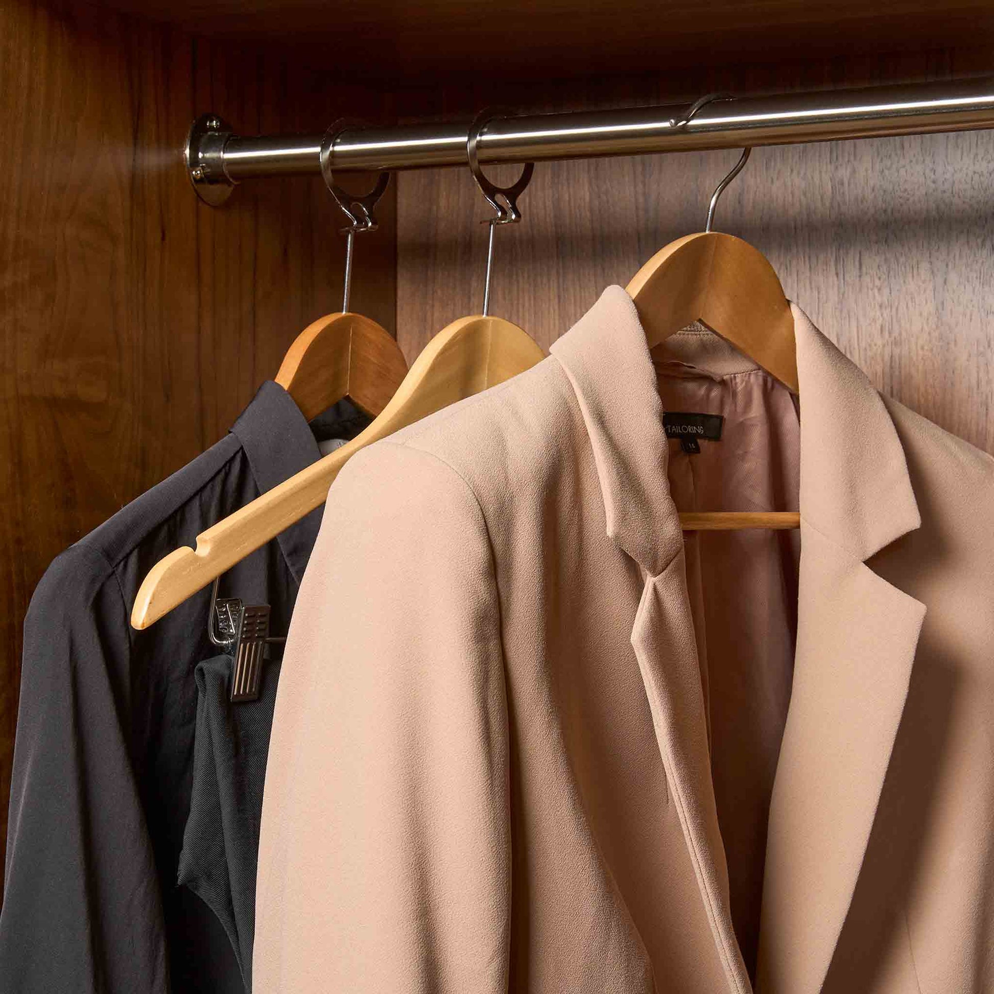 Corby Clifford light wood hotel hangers with chrome hooks holding guest suit and clothing in built-in wardrobe