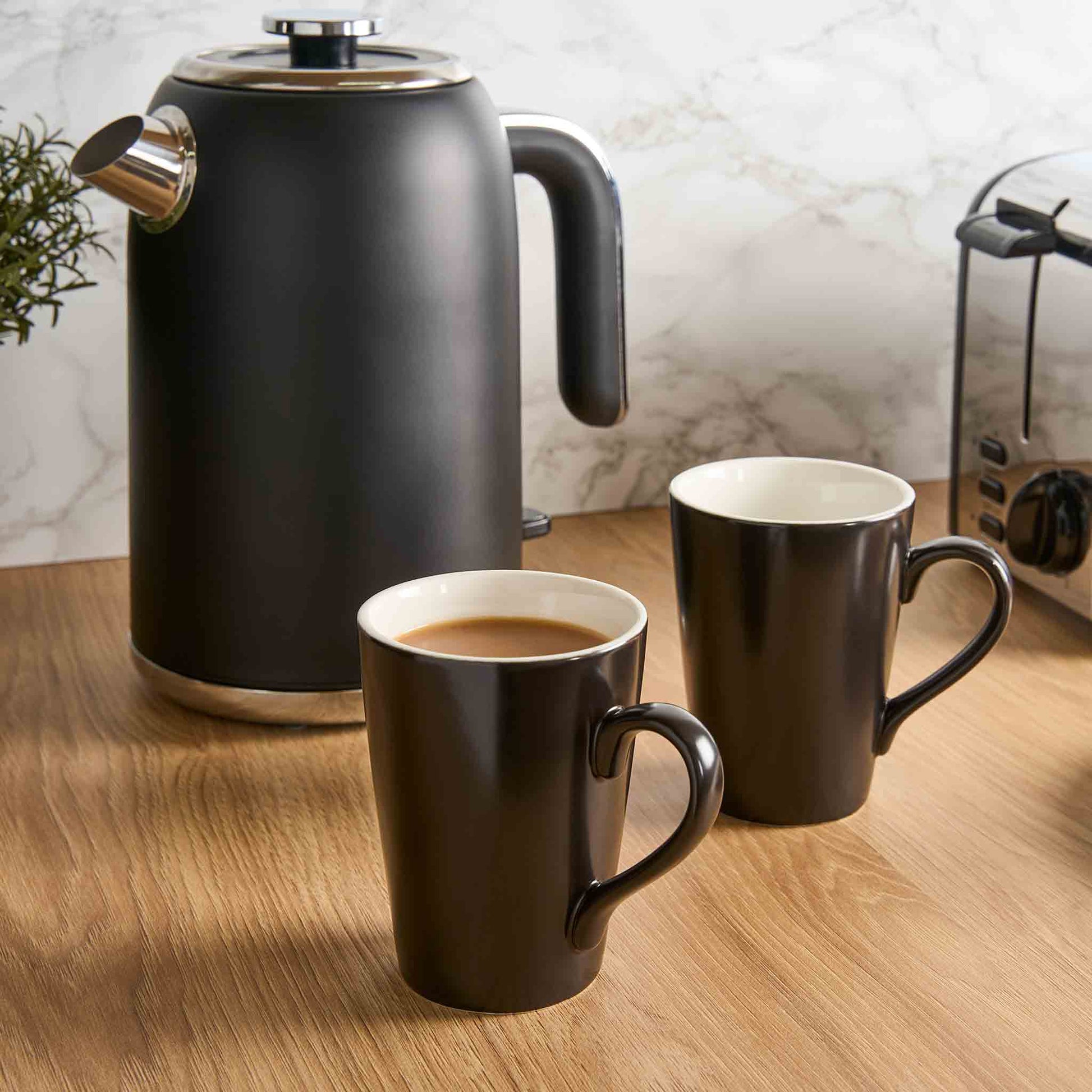Corby Fenton black ceramic mugs with white interior beside matching kettle on wooden countertop in hotel guest refreshment setup