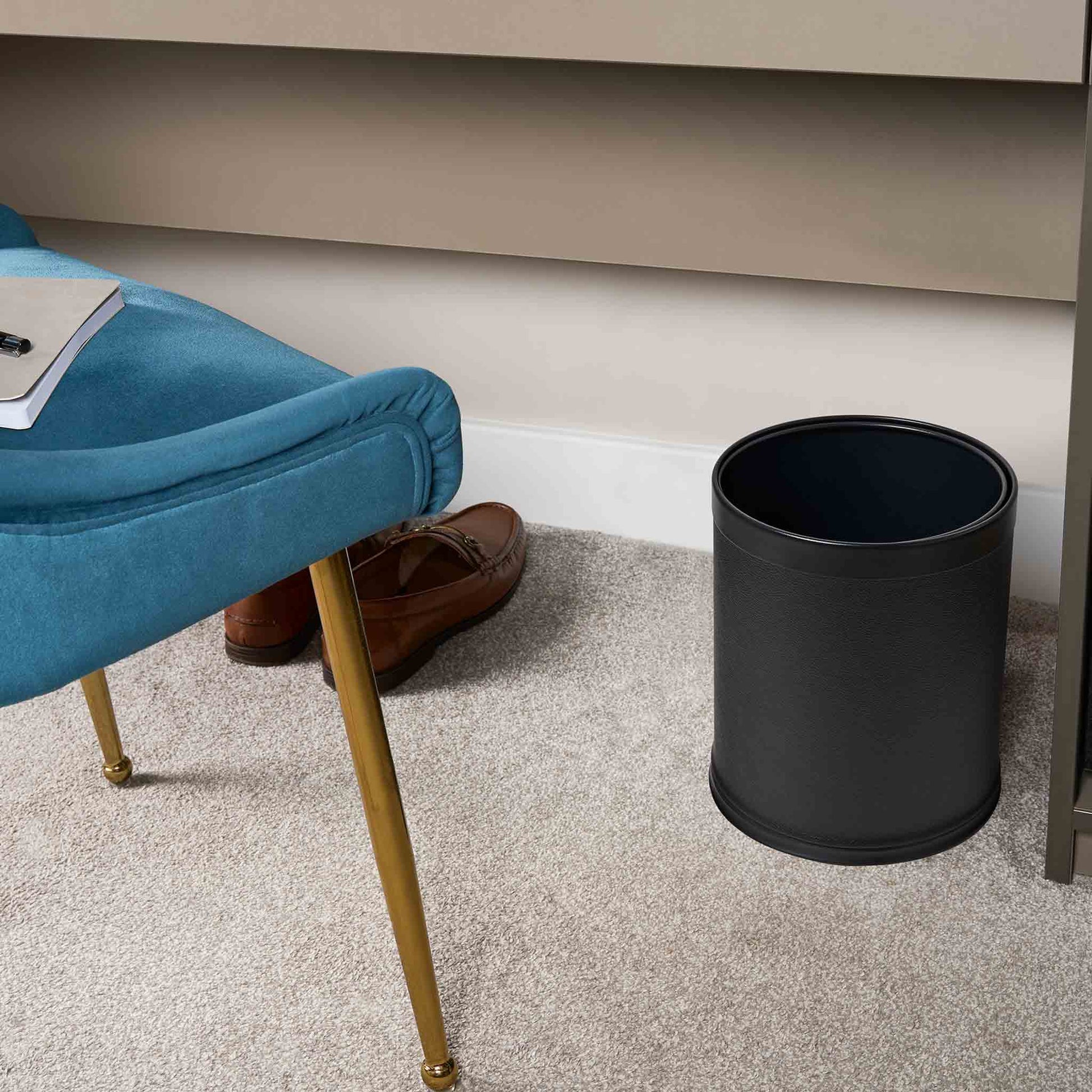 Black trash can next to a blue chair with brown shoes on a carpeted floor.