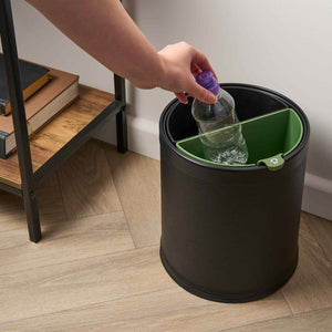 Person disposing of a plastic bottle into a black trash can with a green interior.