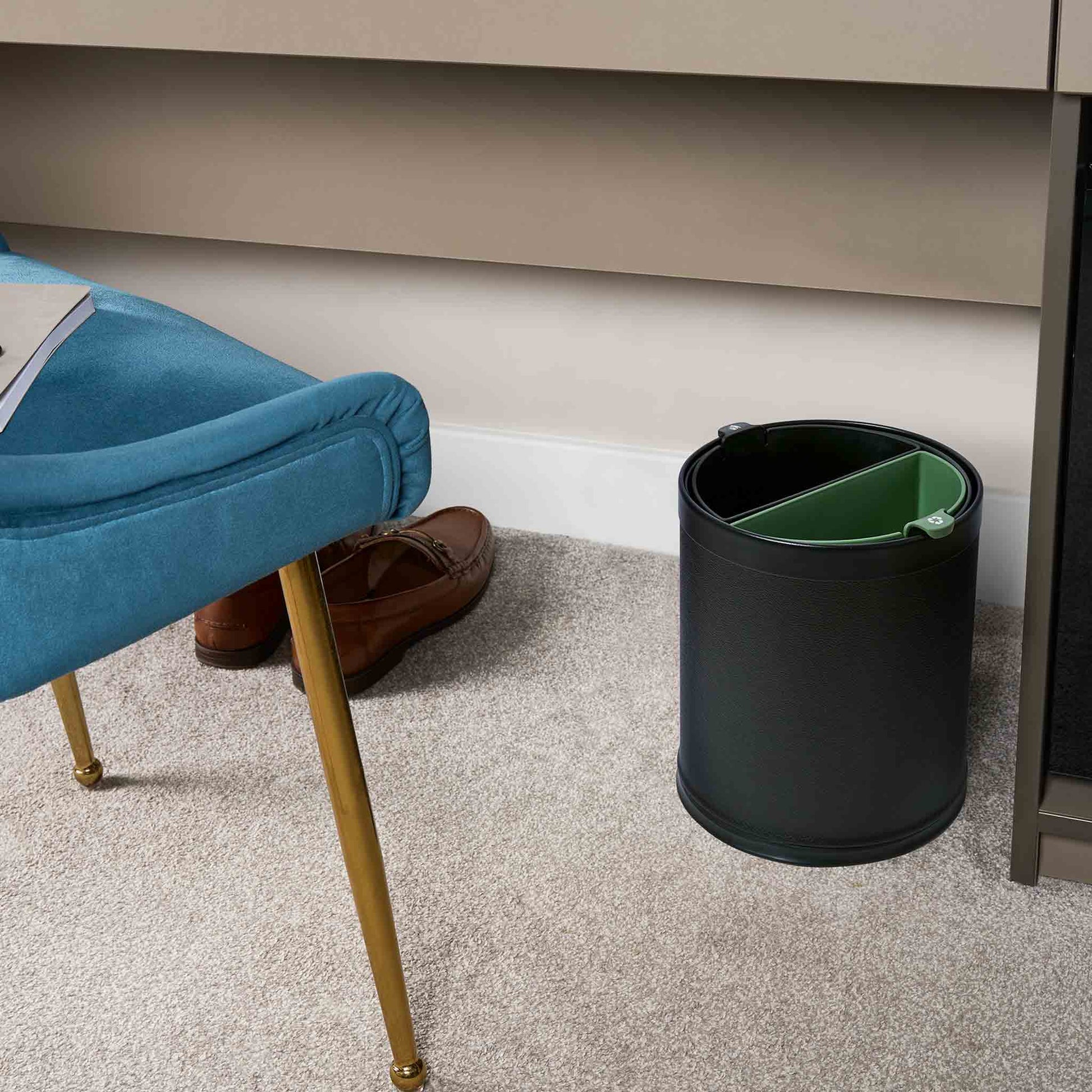 Black trash can with recycling inserts next to a blue chair and brown shoes on a carpeted floor.