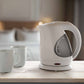 Corby Lancaster 1L white kettle with clear water gauge on a light wooden table in hotel room with two ceramic mugs