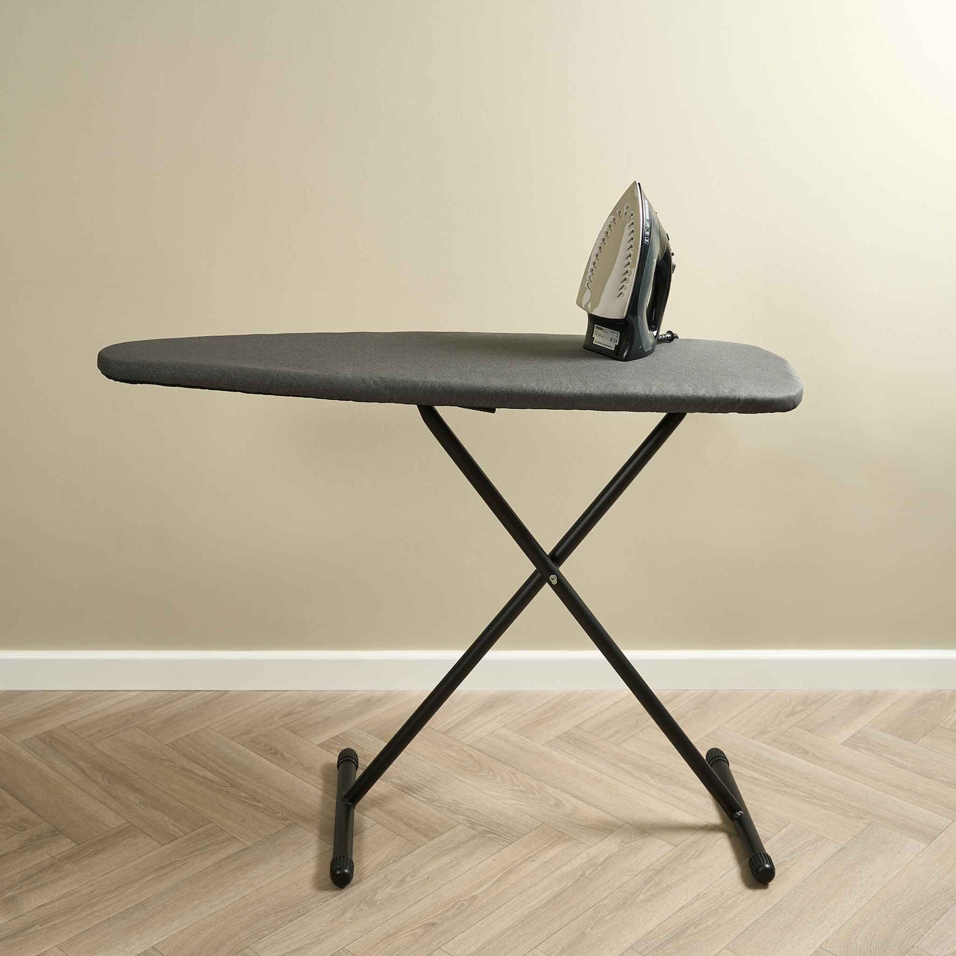 Corby Oxford dark grey ironing board with hotel room iron, set up on wooden floor with neutral wall backdrop