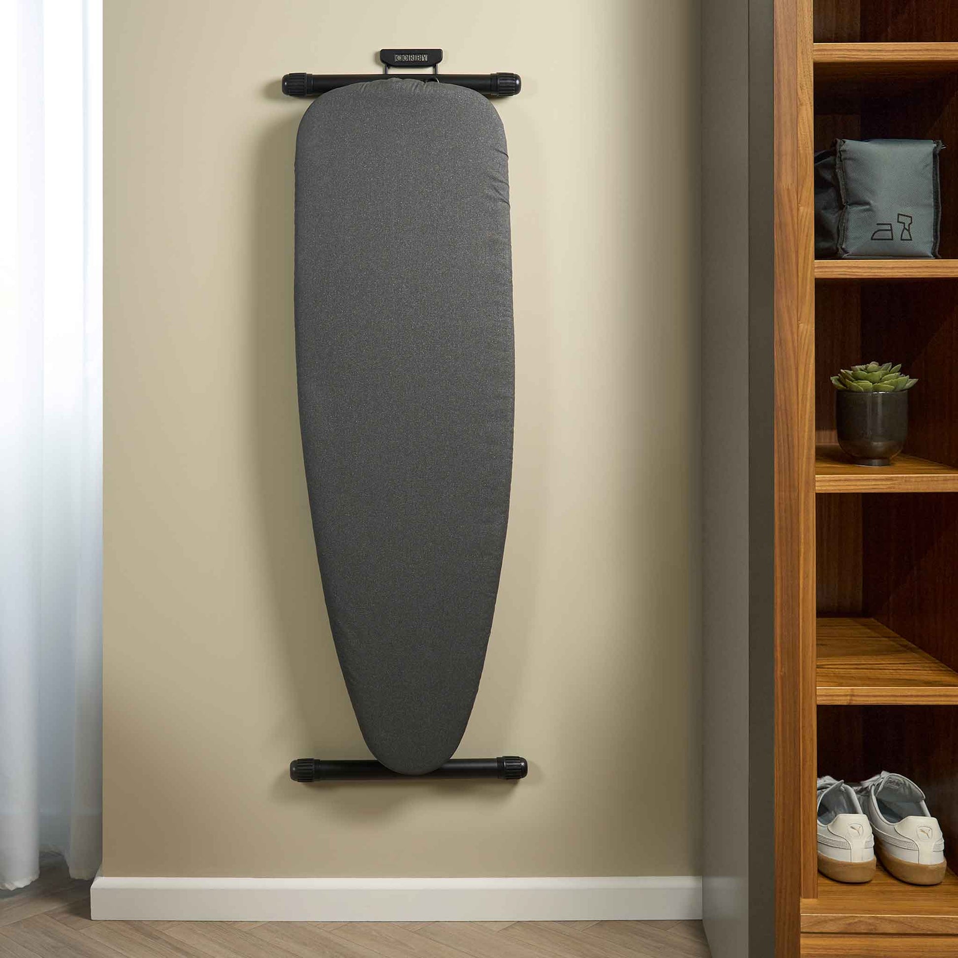 Corby Oxford dark grey ironing board wall-mounted in hotel guest room beside open wardrobe with guest amenities