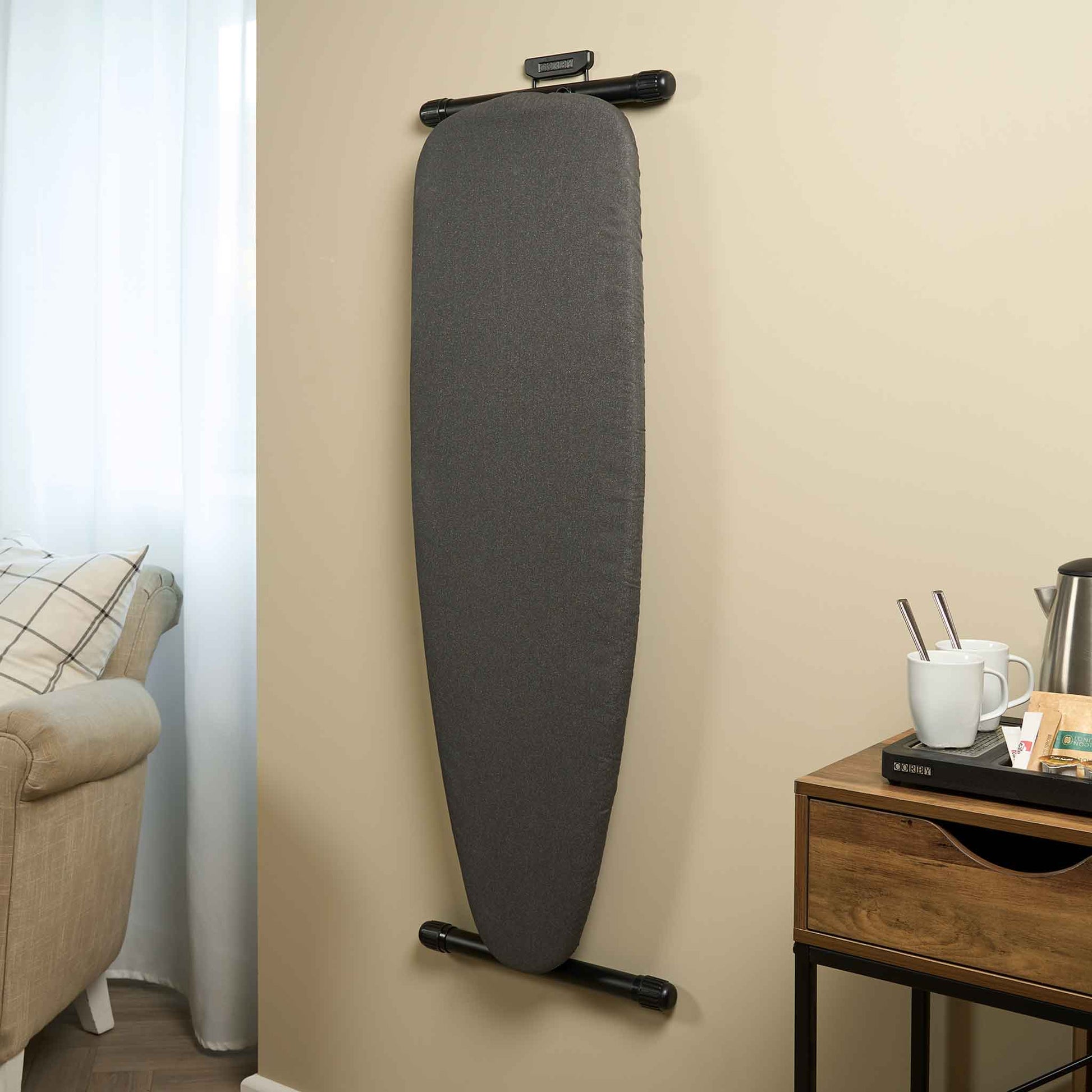 Corby Sherwood dark grey ironing board mounted on wall using branded holder in hotel guest room with coffee tray and armchair