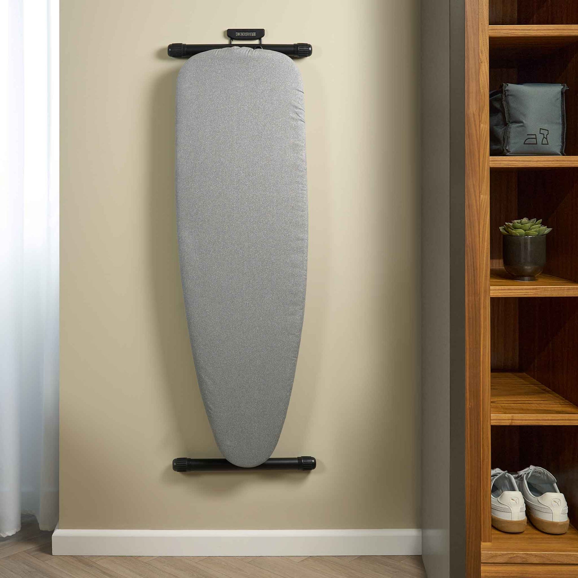 Corby Sherwood light grey ironing board mounted on hotel room wall using black holder, next to open wardrobe shelving