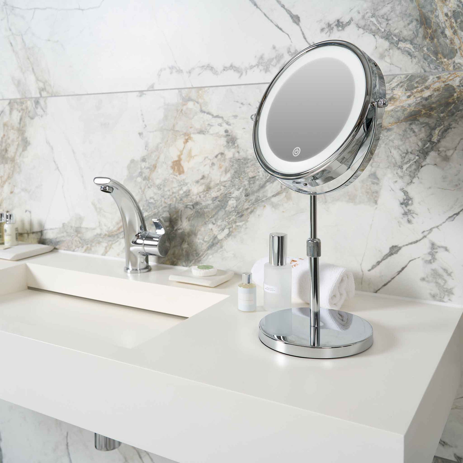Corby Winchester LED vanity mirror with chrome finish on hotel bathroom countertop beside toiletries, towel, and chrome tap