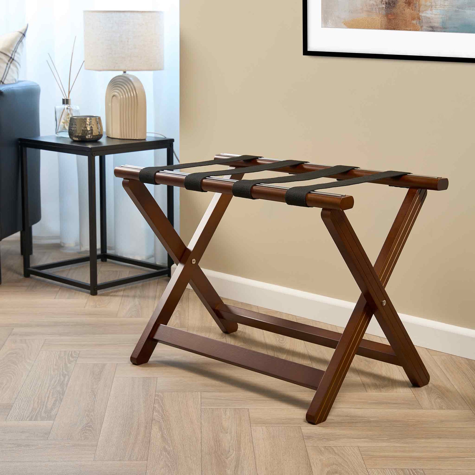 Corby York dark wood luggage rack with black support straps in hotel guest room beside bedside table