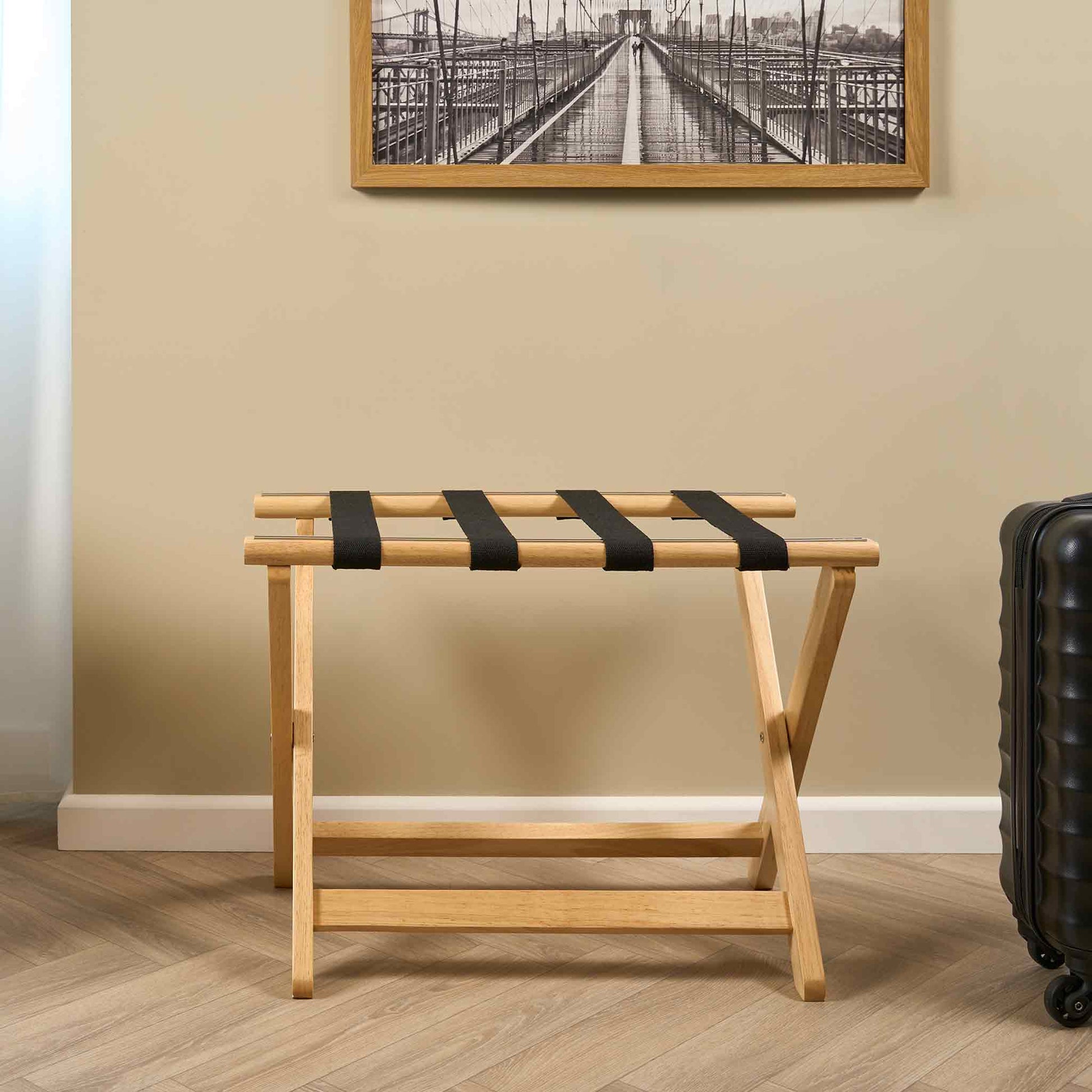 Corby York light wood luggage rack with black straps in hotel guest room beside suitcase