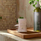 Bottle of liquid hand soap and a bar of soap on a wooden tray with a neutral background
