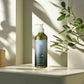Geneva Green 370ml hair and body wash in recycled plastic pump bottle, placed on hotel bathroom shelf with natural light and greenery