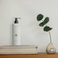 Geneva Guild body moisturiser 380ml pump dispenser placed on books beside sculptural vase and eucalyptus stem in a minimalist hotel or spa setting