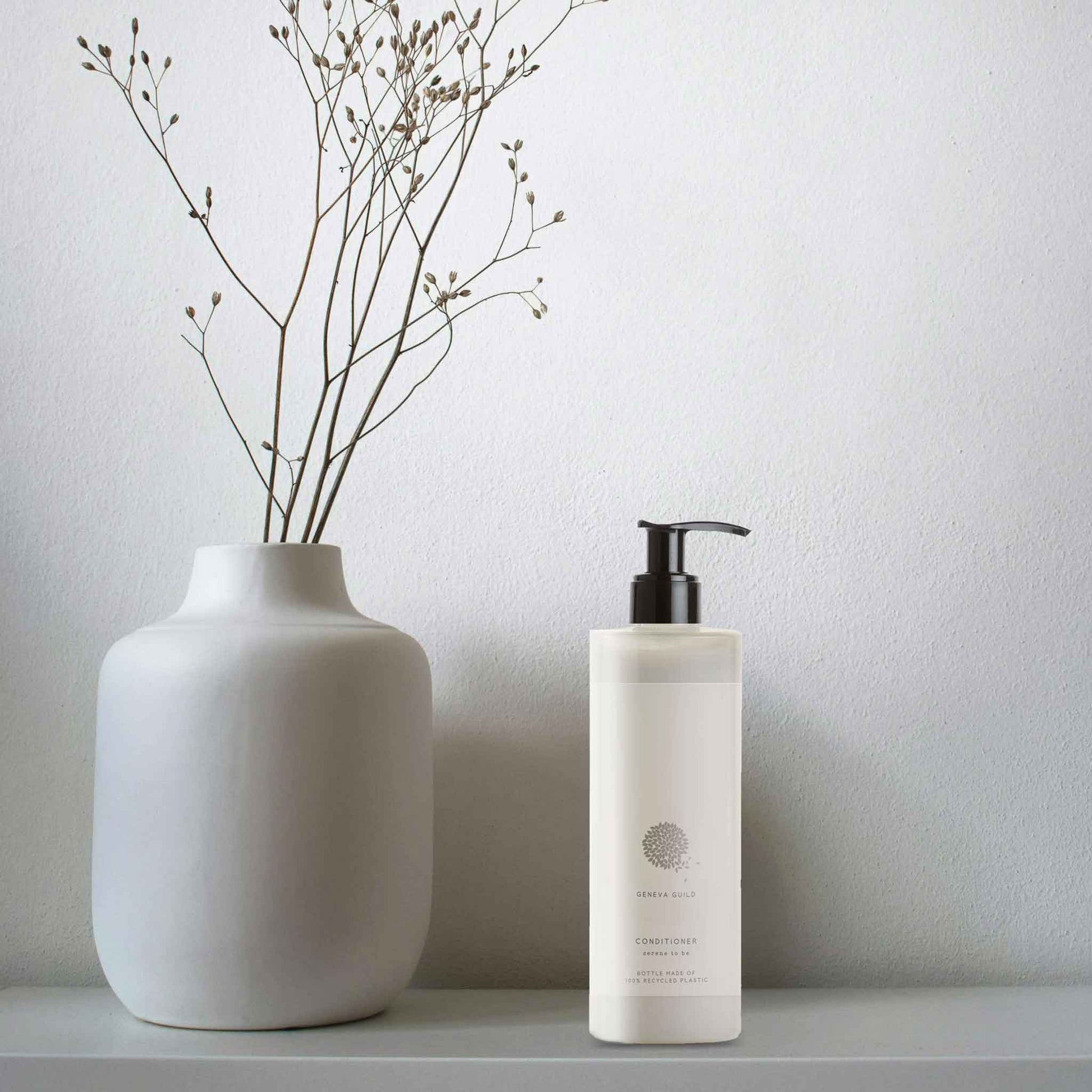 Geneva Guild conditioner 380ml pump bottle placed beside matte ceramic vase with dried stems in minimalist hotel or spa bathroom setting