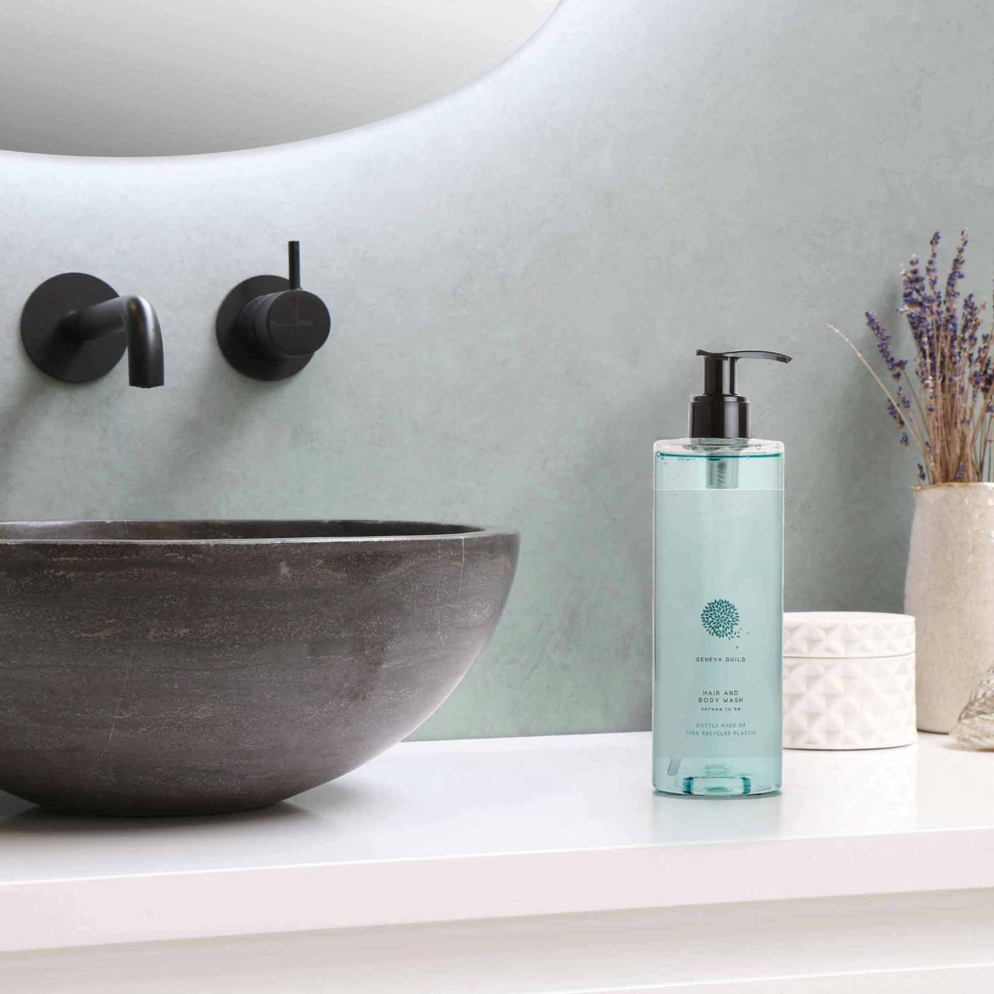 Geneva Guild hair and body wash 380ml pump dispenser placed beside stone basin in contemporary hotel bathroom with black wall-mounted tapware