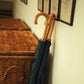Two wooden-handled umbrellas, one dark green and one dark blue, leaning against a cream-colored wall next to a wicker storage basket.