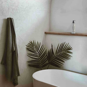 Bathroom with a green towel hanging, a white bathtub, and a shelf with a bottle.