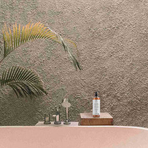 Bathroom setting with a bottle on a wooden block against a textured wall with palm leaves.