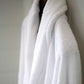 A close-up of a white terry towelling bathrobe hanging against a light neutral wall.