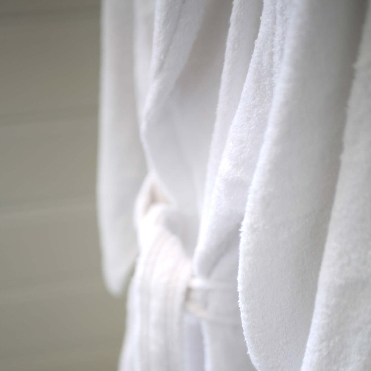 A close-up of a white terry towelling bathrobe with a matching belt, showing the soft texture of the fabric.